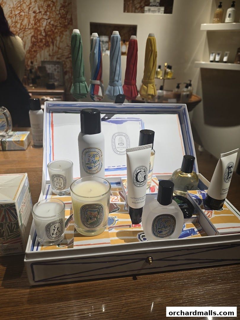A display of Diptyque scented candles, lotions, and perfumes in a decorative box.