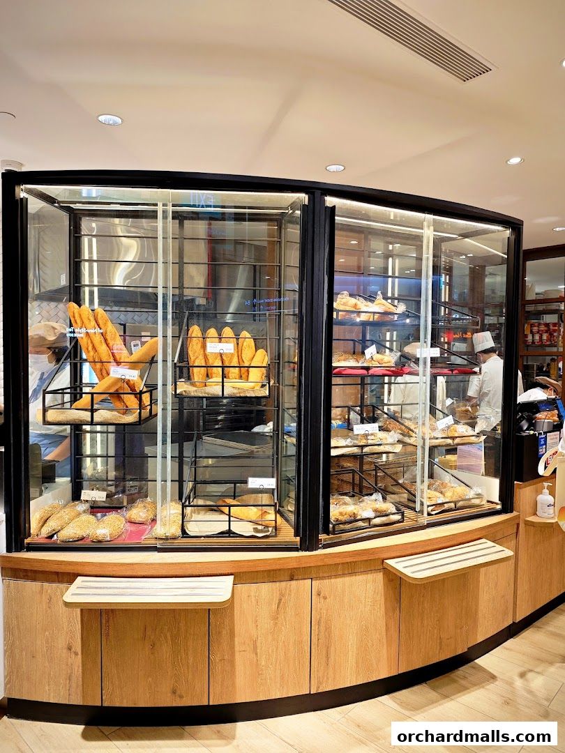 A display case filled with various types of bread and pastries at a bakery.