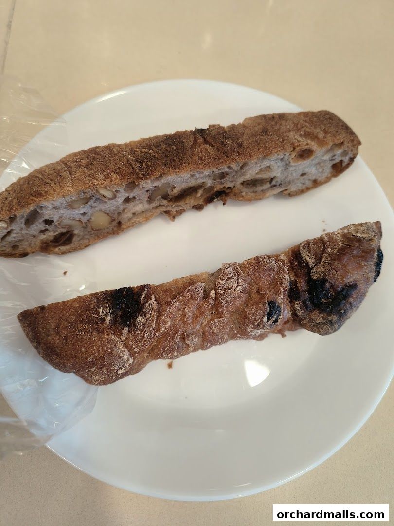 Two pieces of artisanal bread with nuts and dried fruit on a white plate.