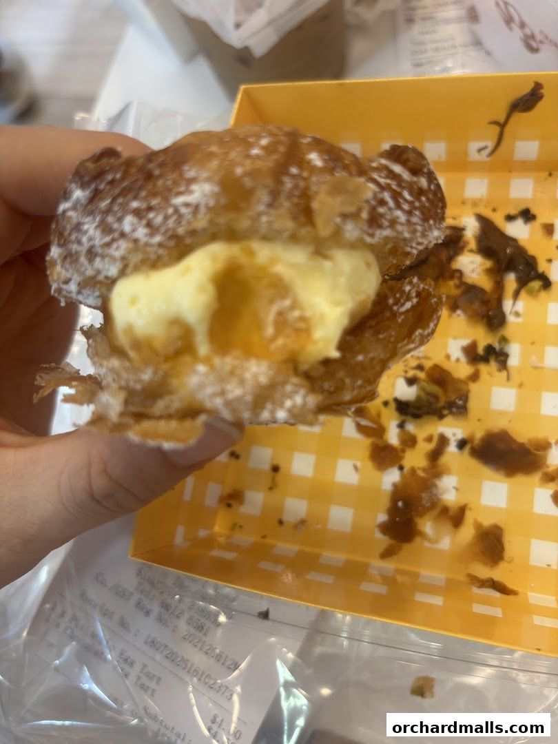 A person holds a cream-filled pastry dusted with powdered sugar in a yellow checkered box.