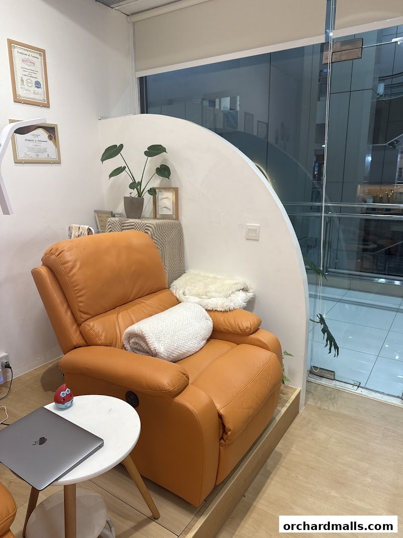 A comfortable orange recliner chair with a laptop on a side table in a beauty studio.