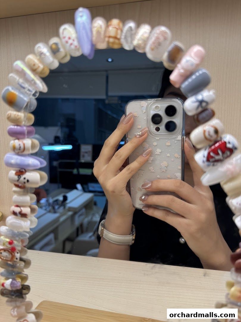 A person takes a selfie in a mirror displaying various nail art designs.