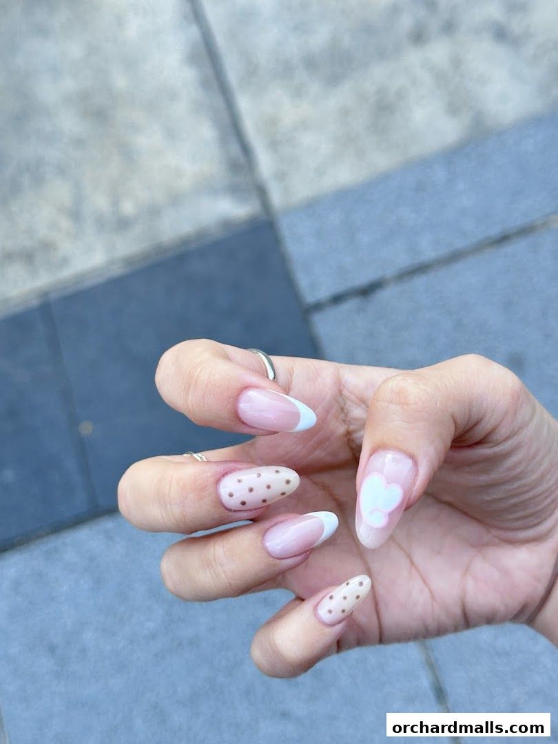 A close-up of a hand showcasing beautifully manicured nails with French tips and cute polka dot designs.