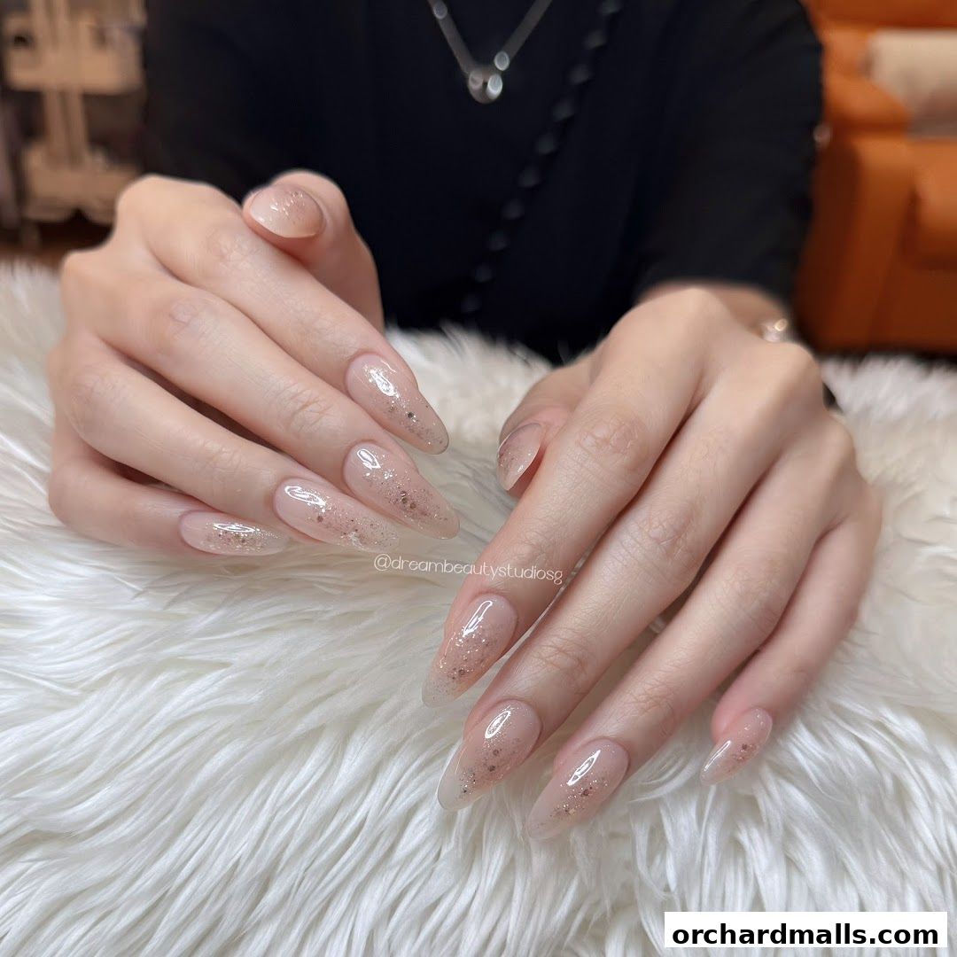 Close-up of elegant, long, almond-shaped nails with subtle glitter accents.