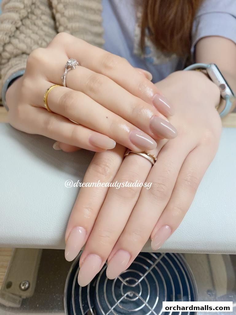 Close-up of a woman's hands with elegant, nude-colored almond-shaped nails.