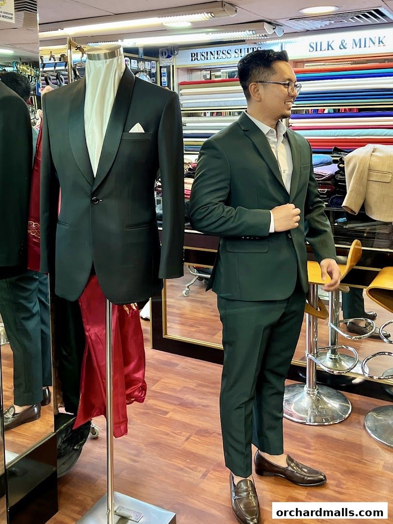 Mannequin and man in stylish green suits inside a tailor shop.