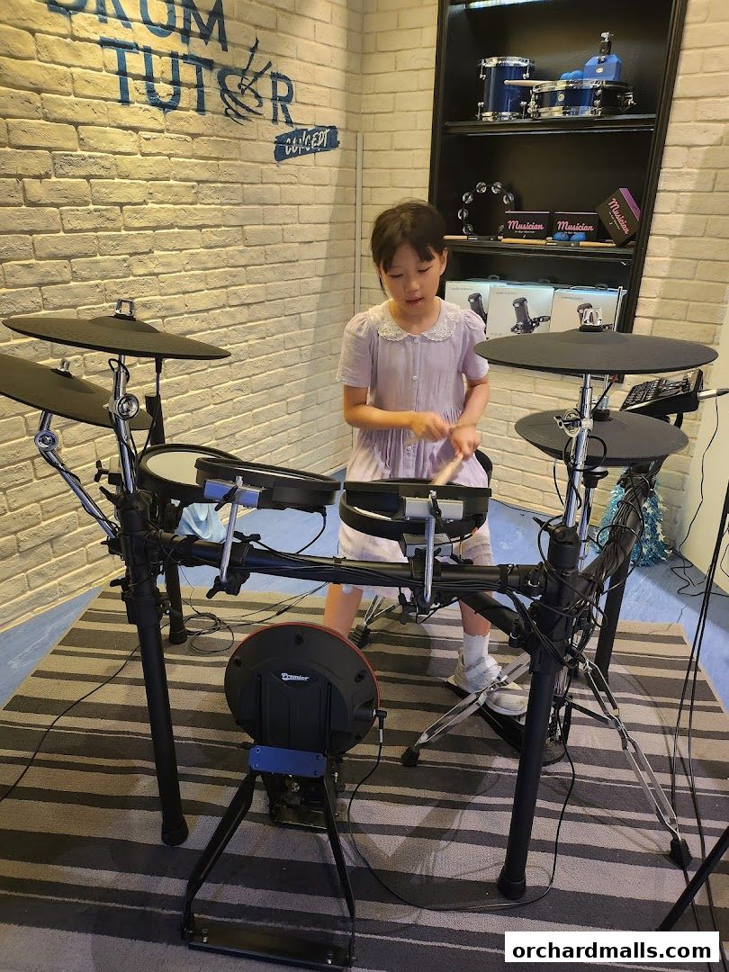 A young girl practices drumming on an electronic drum set in a studio.