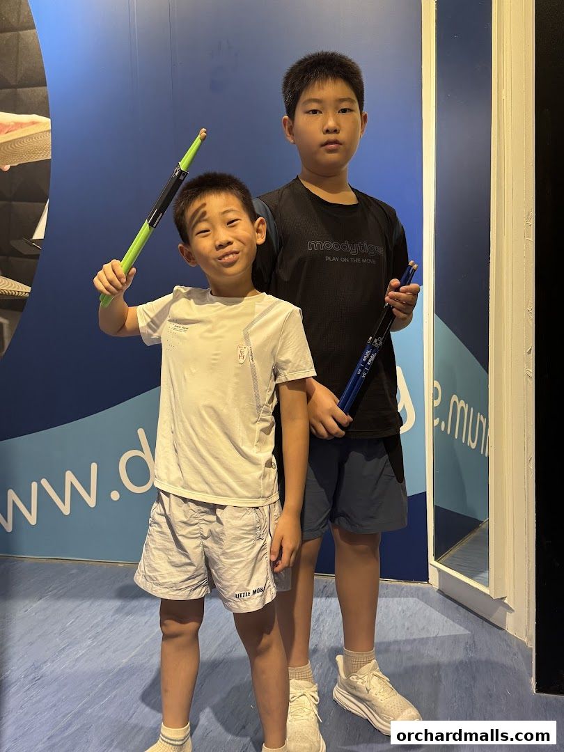 Two young boys holding drumsticks in front of a blue wall with text.