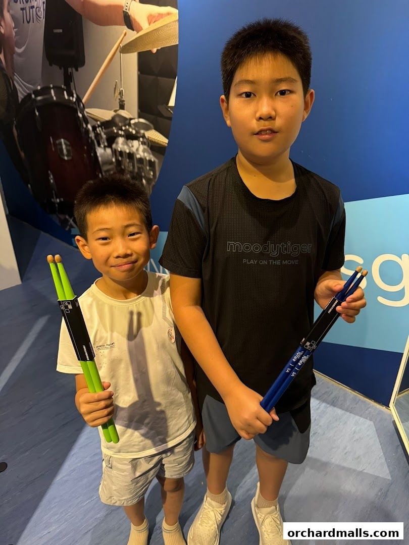 Two young boys proudly hold drumsticks, ready to learn.