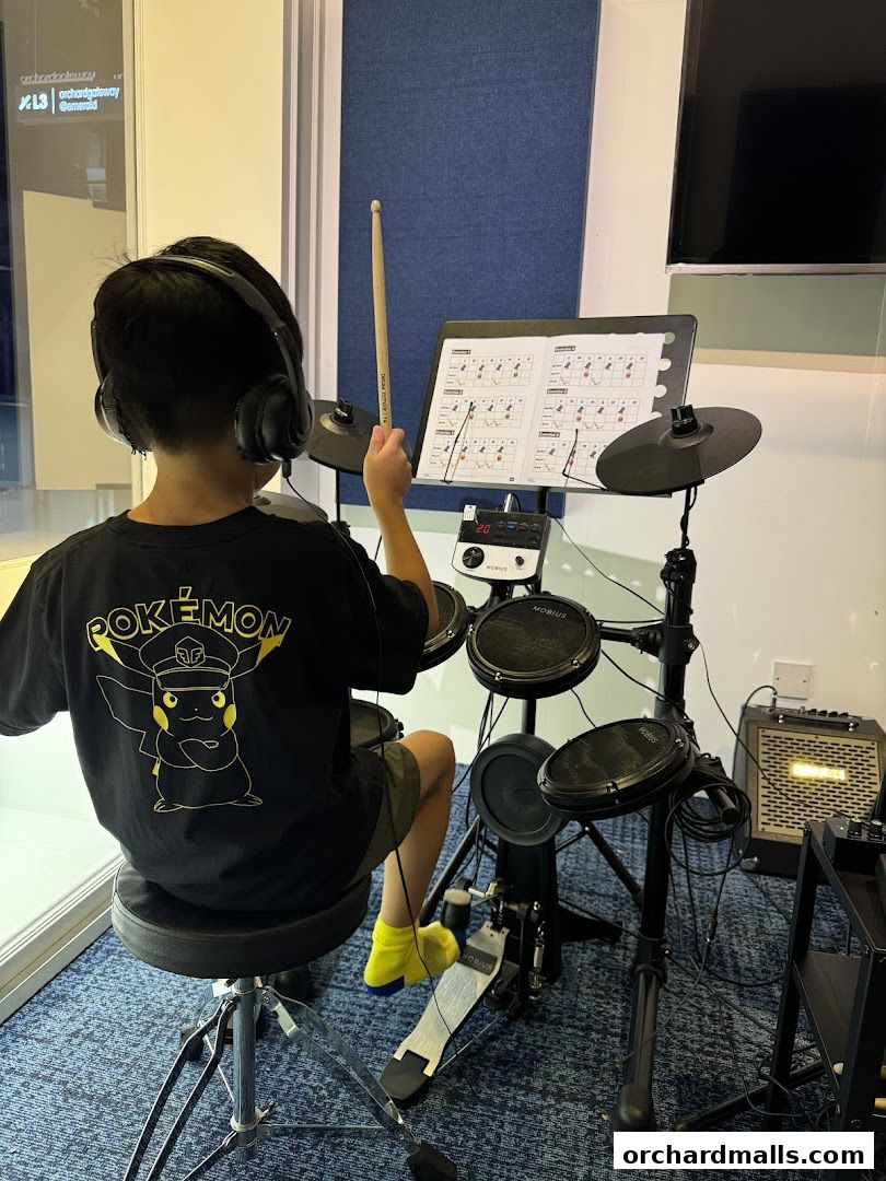 A child wearing headphones plays an electronic drum set while looking at sheet music.