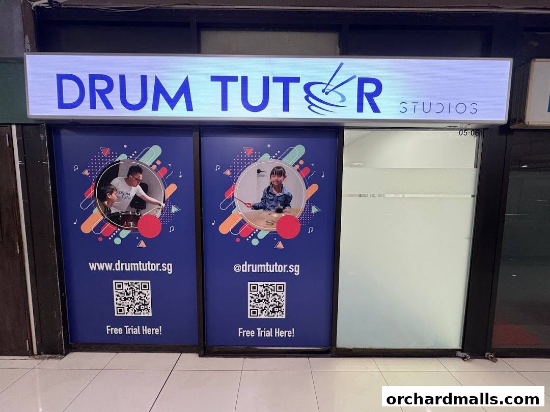 The storefront of Drum Tutor Studios, featuring a large illuminated sign and posters with QR codes.