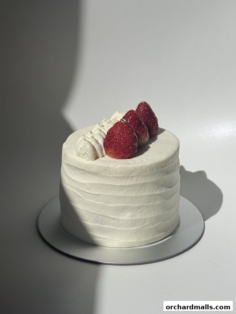 A small, white frosted cake topped with whipped cream and fresh strawberries.