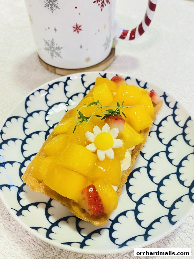 A delicious mango and strawberry tart served on a decorative plate with a festive mug.