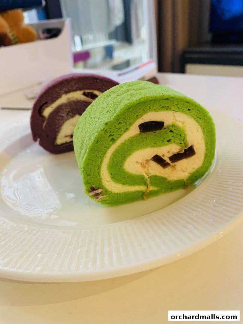 Two delicious swiss rolls, one green and one purple, sit on a white plate.