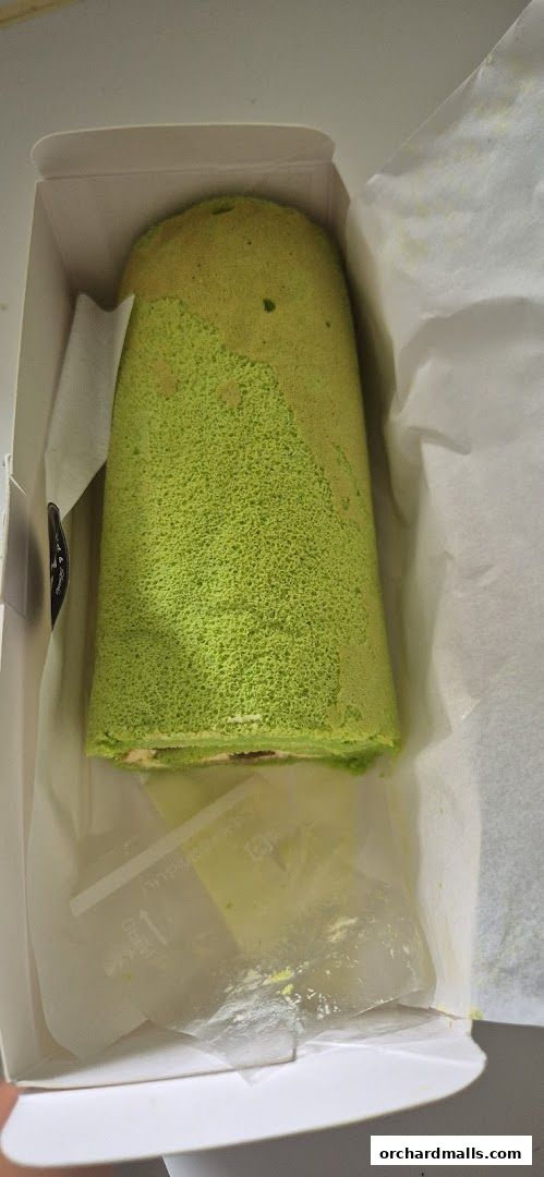 A green matcha swiss roll cake in a white box, ready for takeaway.