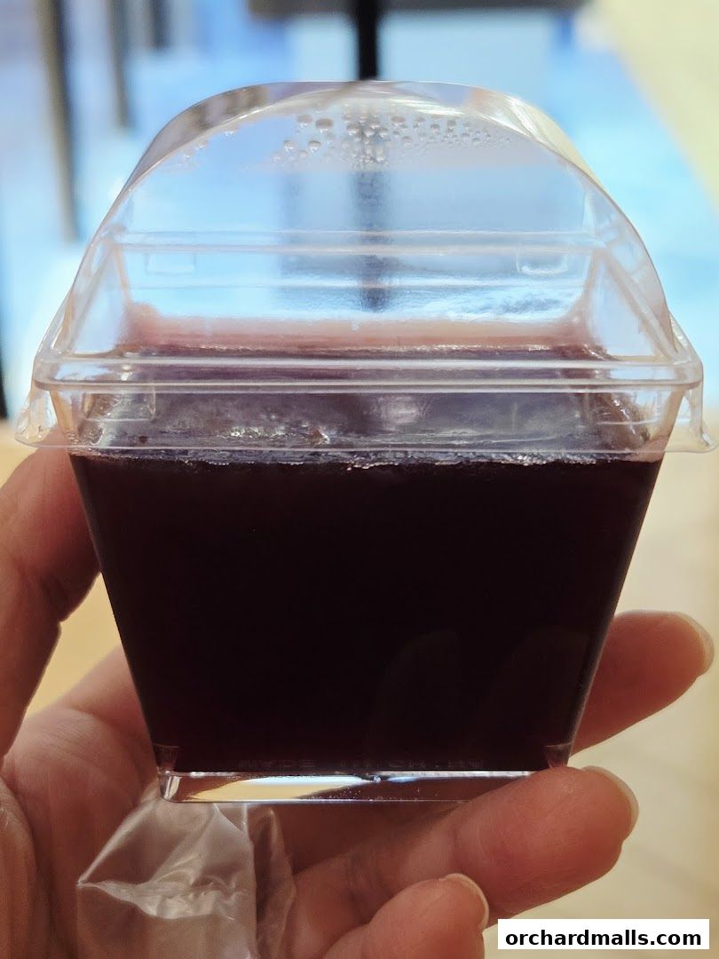 A hand holds a small, clear plastic cup filled with a dark purple liquid.