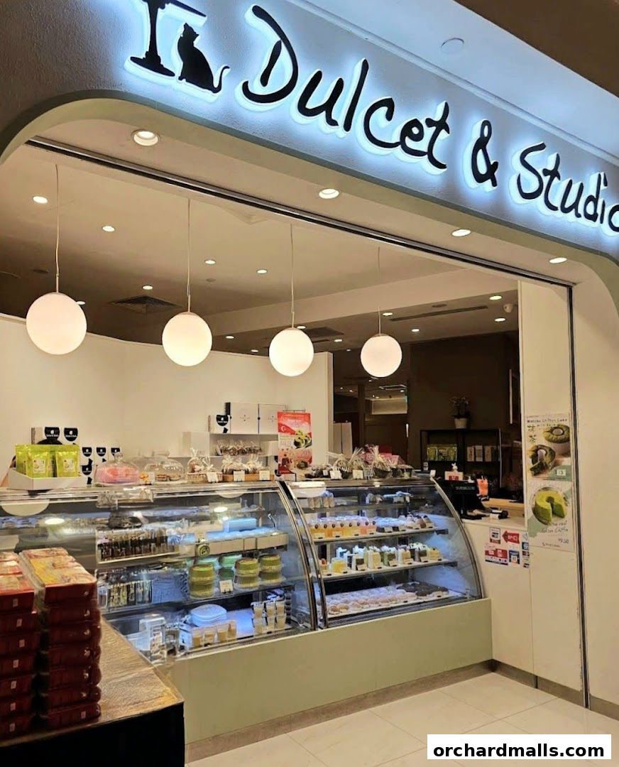 A well-lit bakery display case filled with various cakes and pastries, with the shop name above.