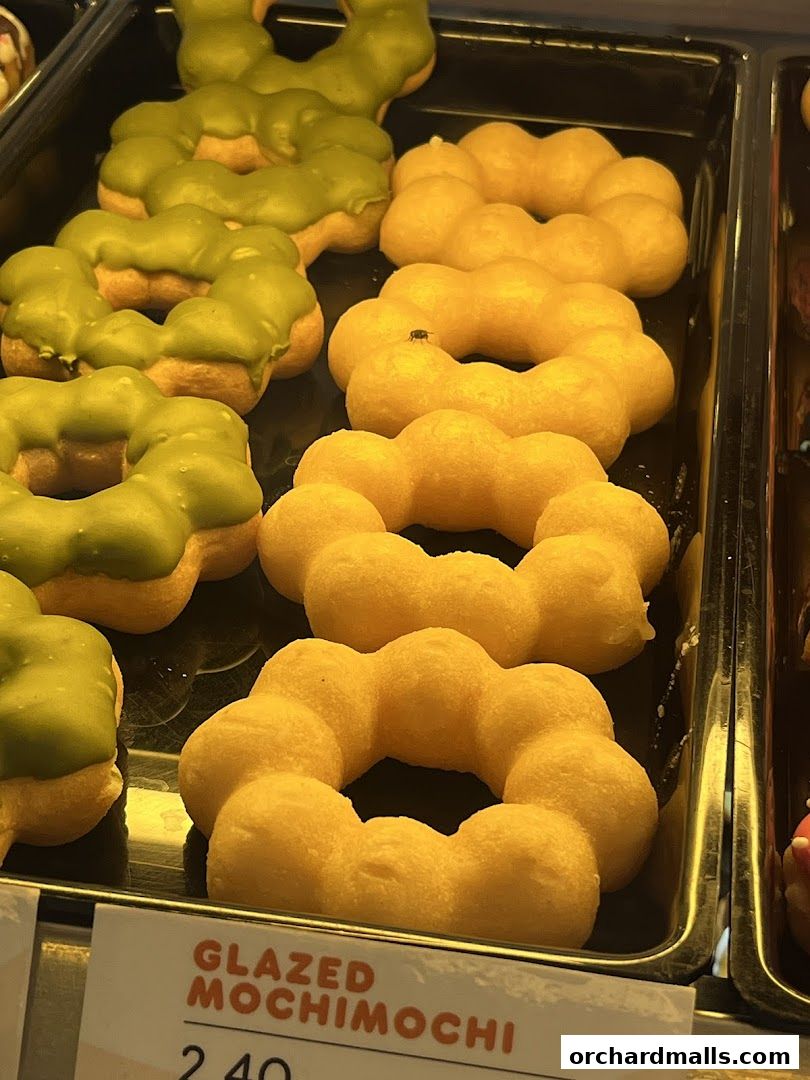 A close-up of green and yellow mochi donuts displayed in a tray.