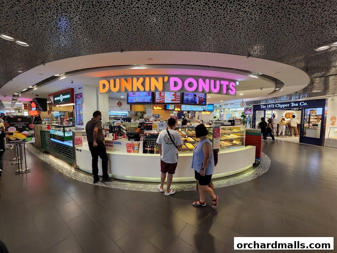 People are standing at the counter of a Dunkin' Donuts shop with display cases full of donuts.