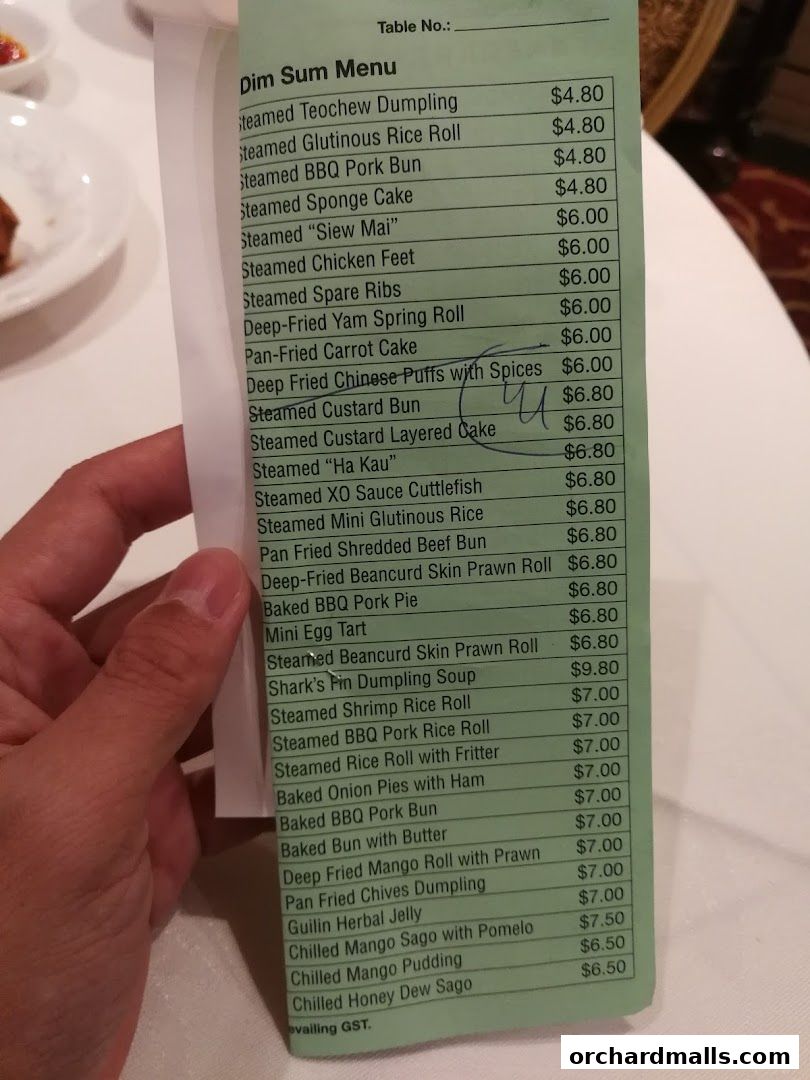 A hand holds a green dim sum menu with various Chinese dishes and prices listed.