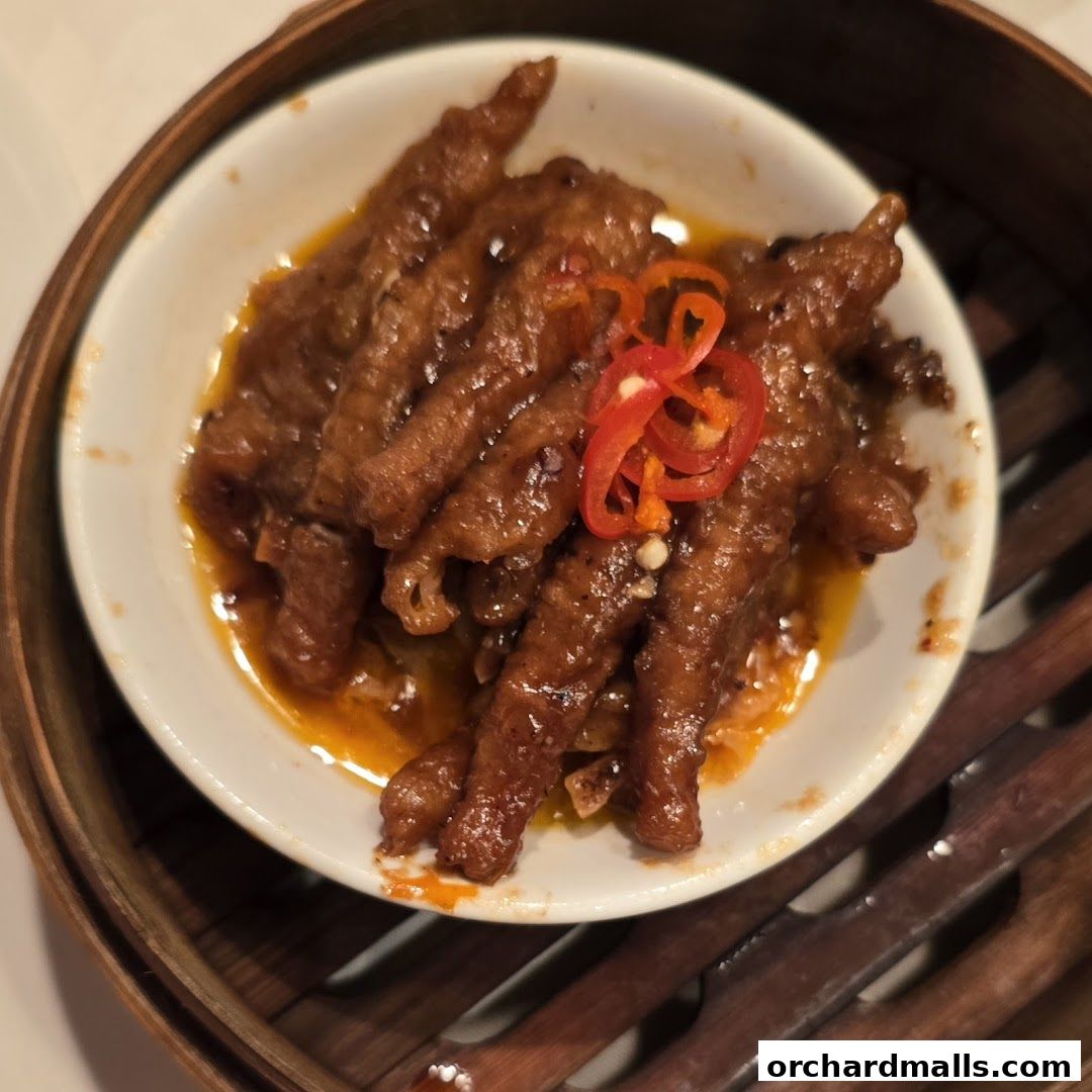 A close-up of braised chicken feet in a savory sauce, garnished with chili slices.