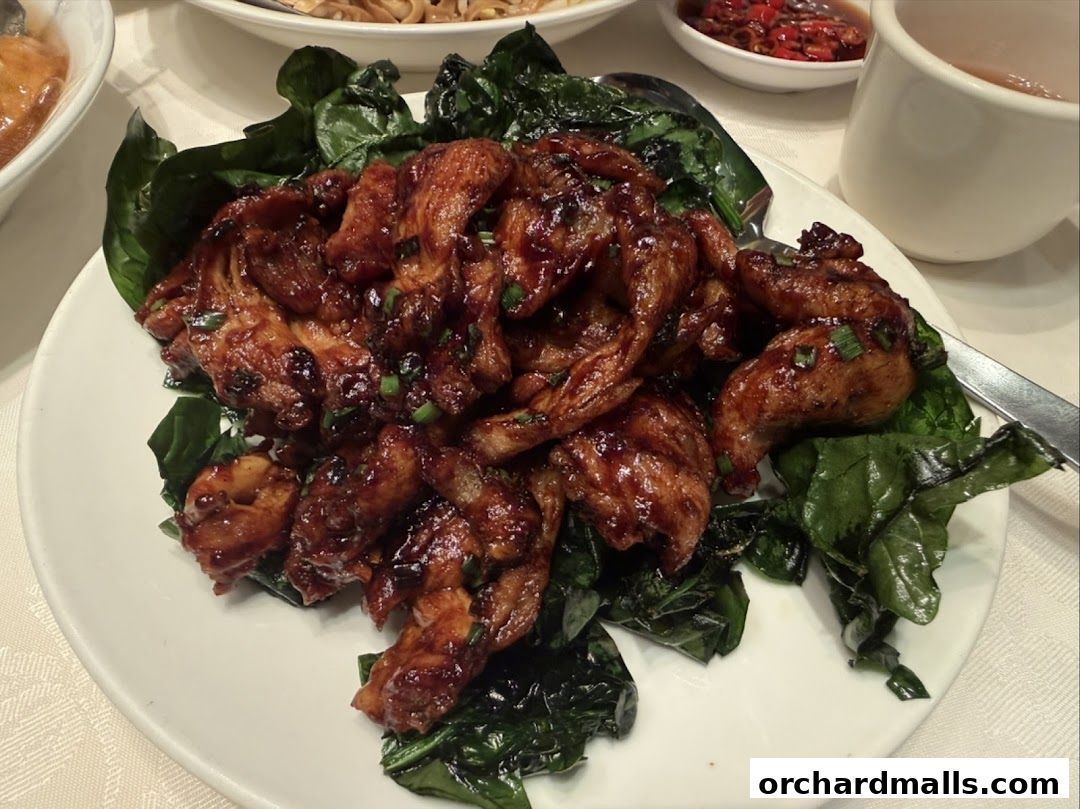 A plate of glistening, glazed chicken wings served with wilted greens.