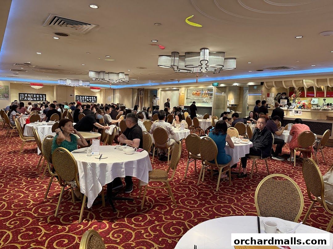 A busy restaurant interior with many diners seated at round tables covered in white tablecloths.