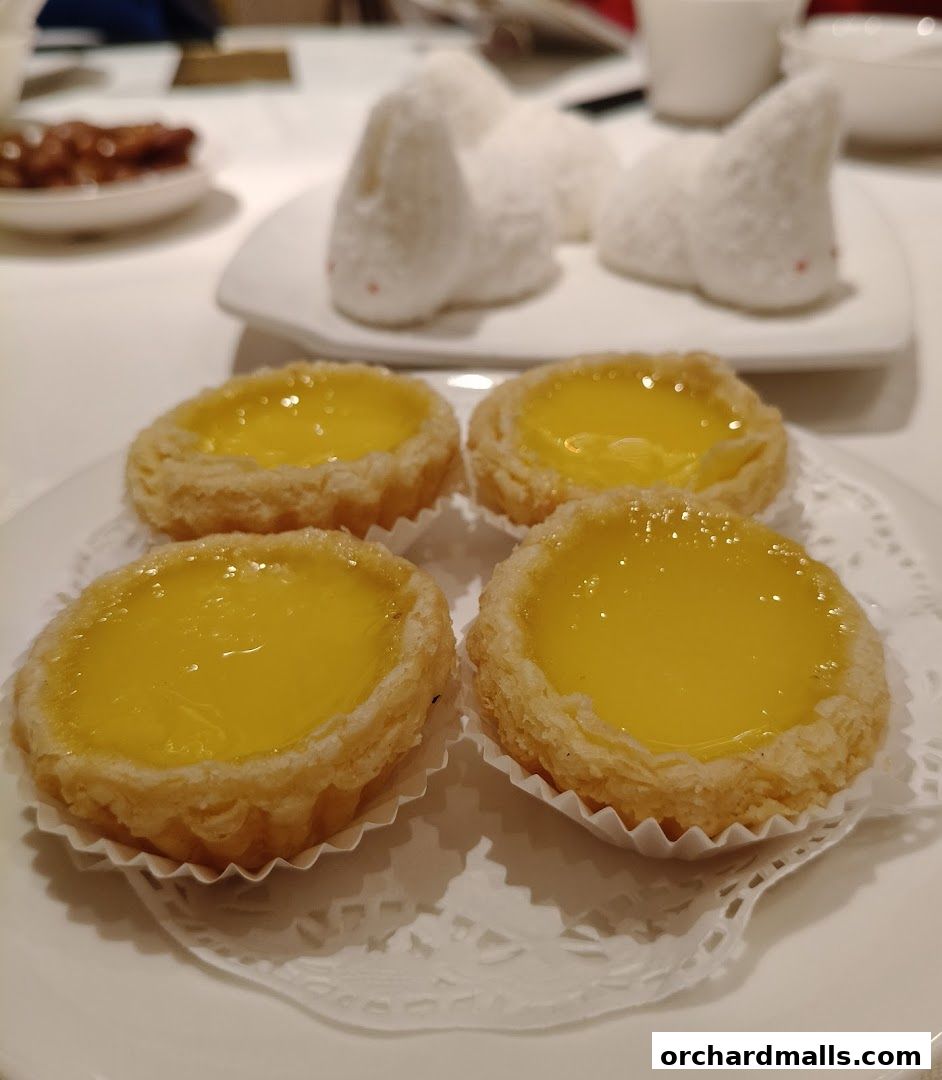 Four golden egg tarts are presented on a white plate with decorative paper liners.