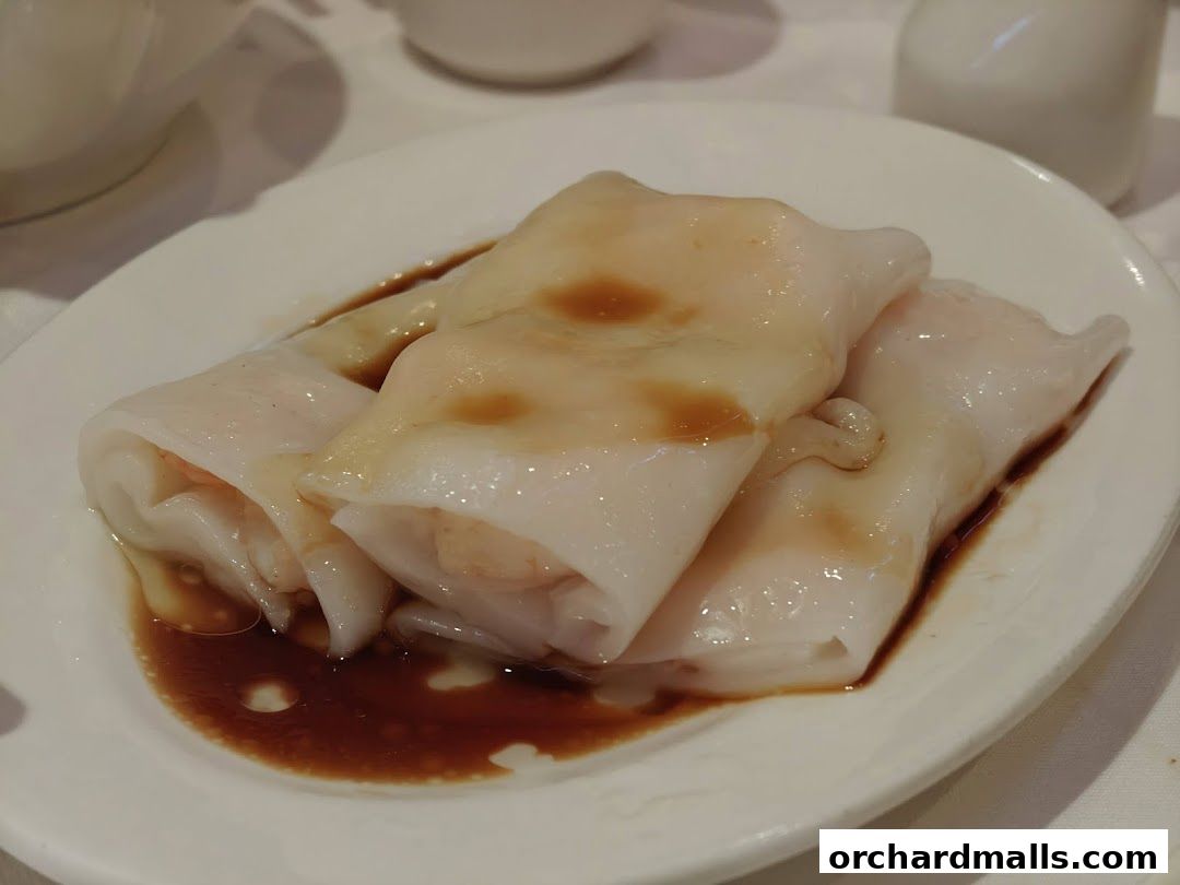 A plate of three steamed rice noodle rolls with shrimp filling, drizzled with soy sauce.