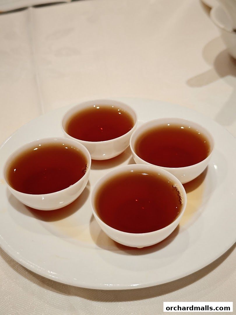 Four small cups of dark tea are served on a white plate.