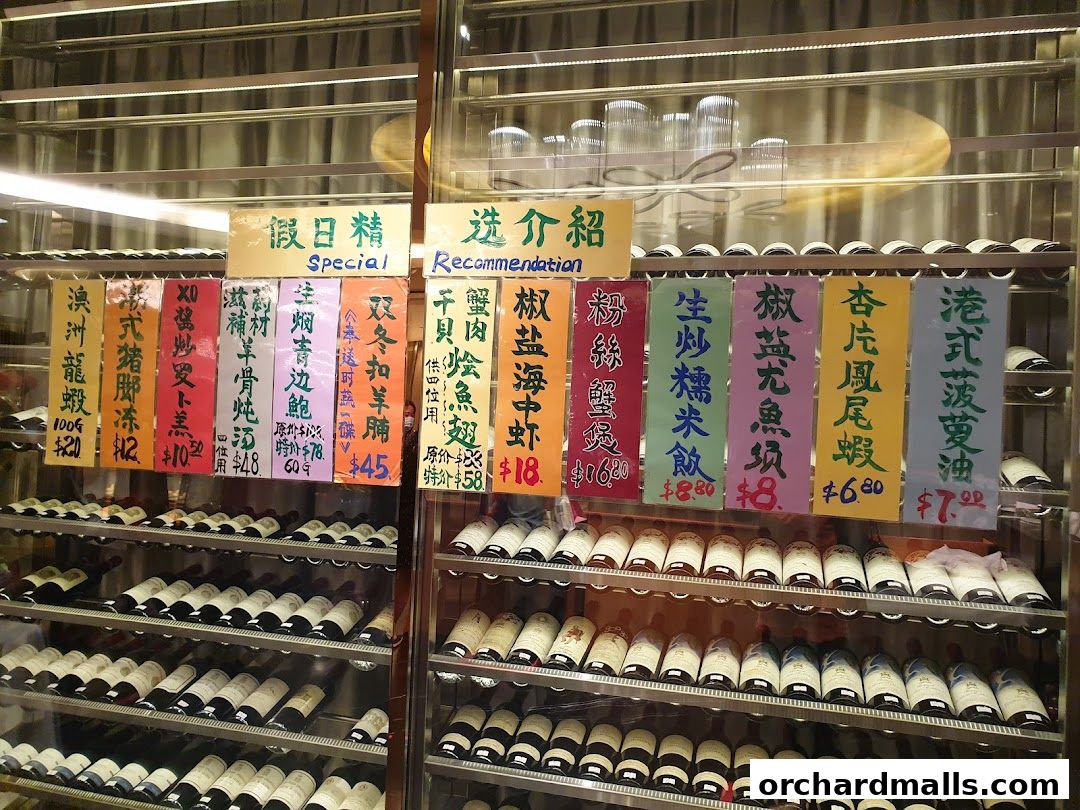 A display case filled with bottles of wine and various food items with prices listed on colorful signs.