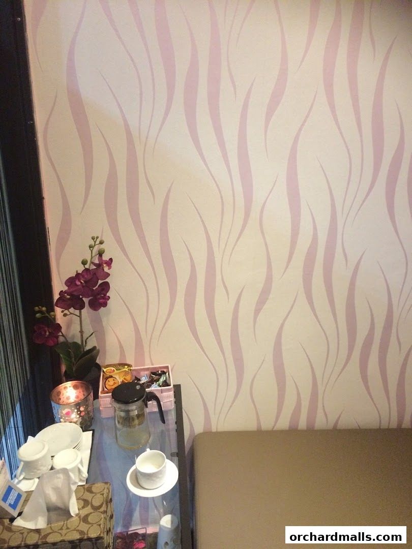 A corner of a room with a patterned wallpaper, a glass table with tea set and flowers.