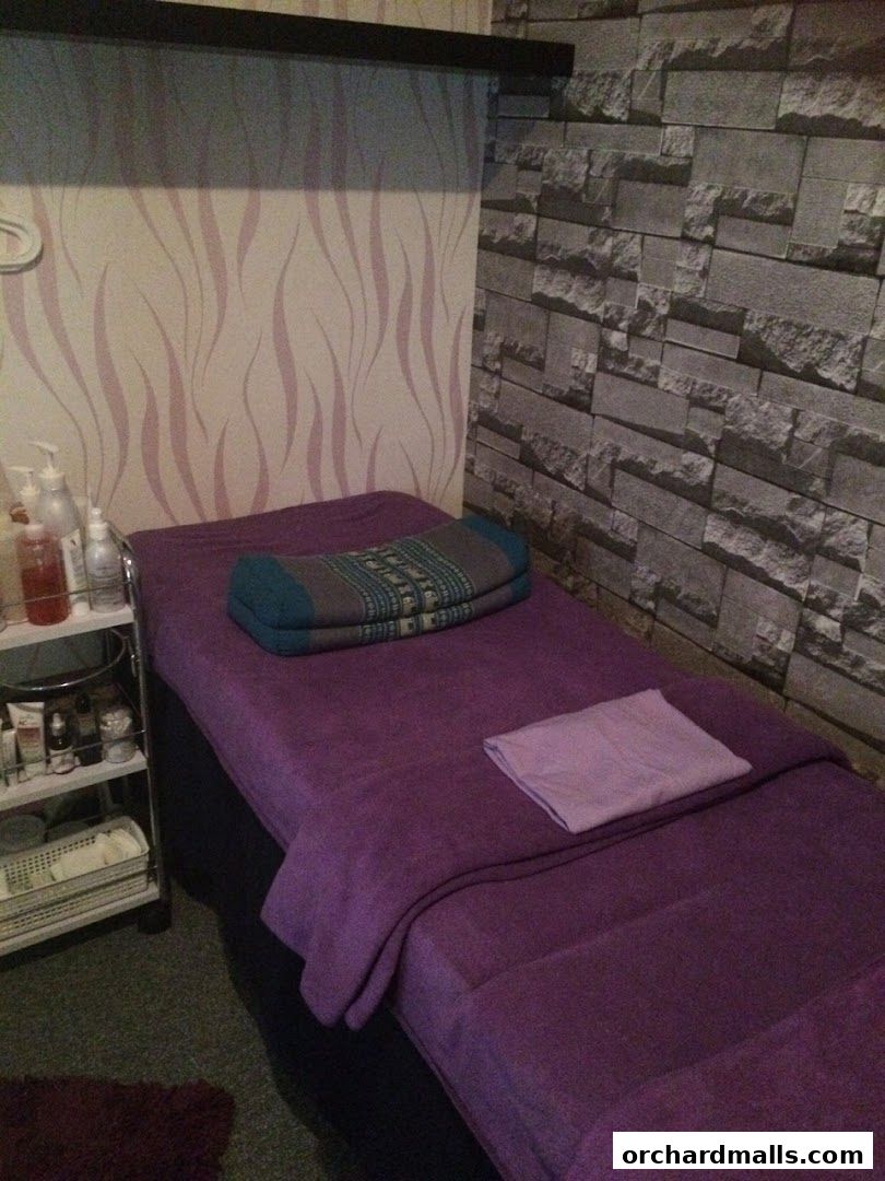 A massage bed with purple linens and a bolster, next to a shelf of products.