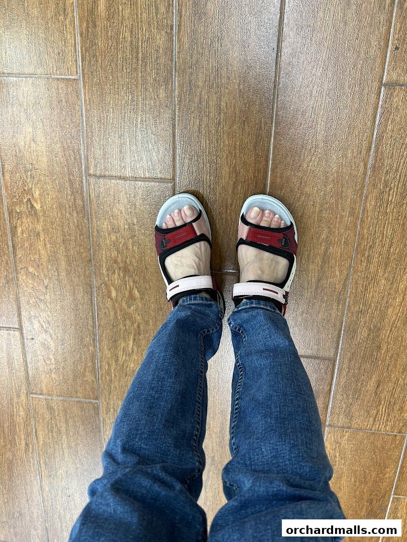 A person wearing ECCO sandals and blue jeans standing on a wooden floor.