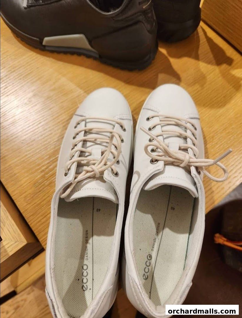 A pair of white ECCO sneakers and a pair of black ECCO sneakers on a wooden surface.