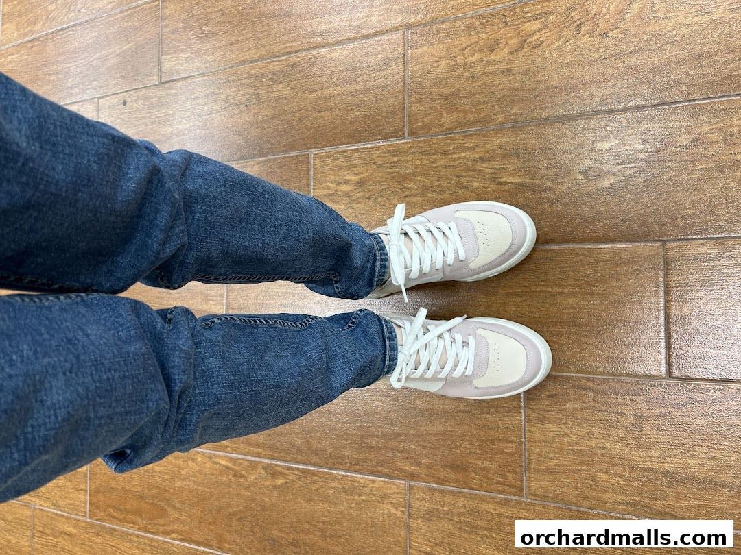 A person wearing ECCO sneakers and blue jeans standing on a wooden floor.