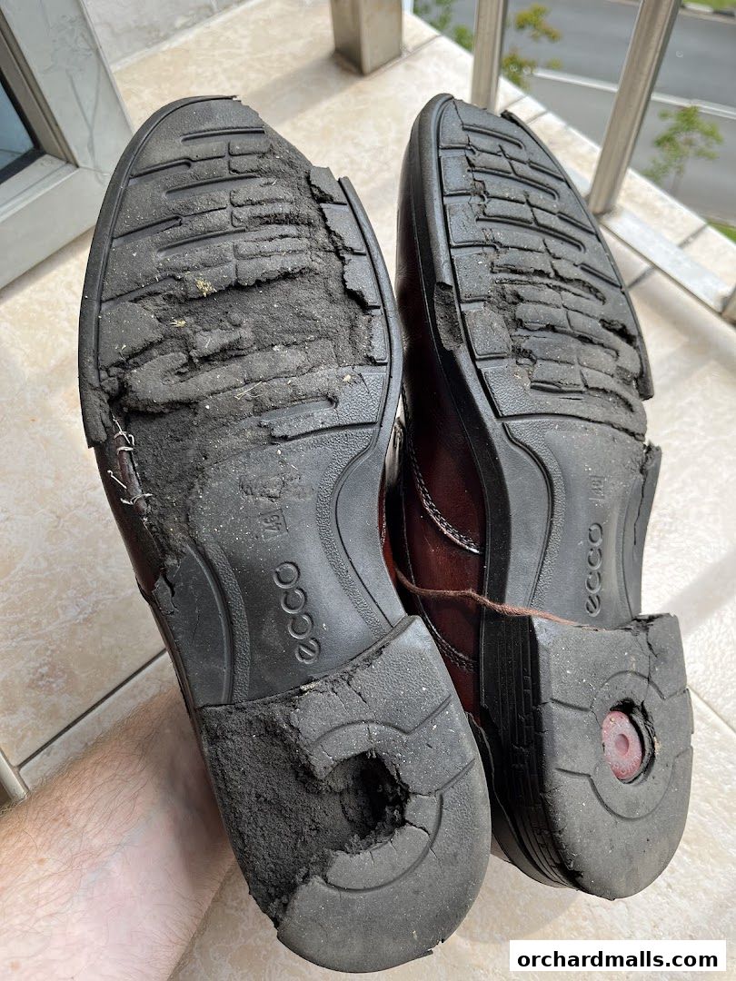 Close-up of the heavily worn and damaged soles of two ECCO leather shoes.