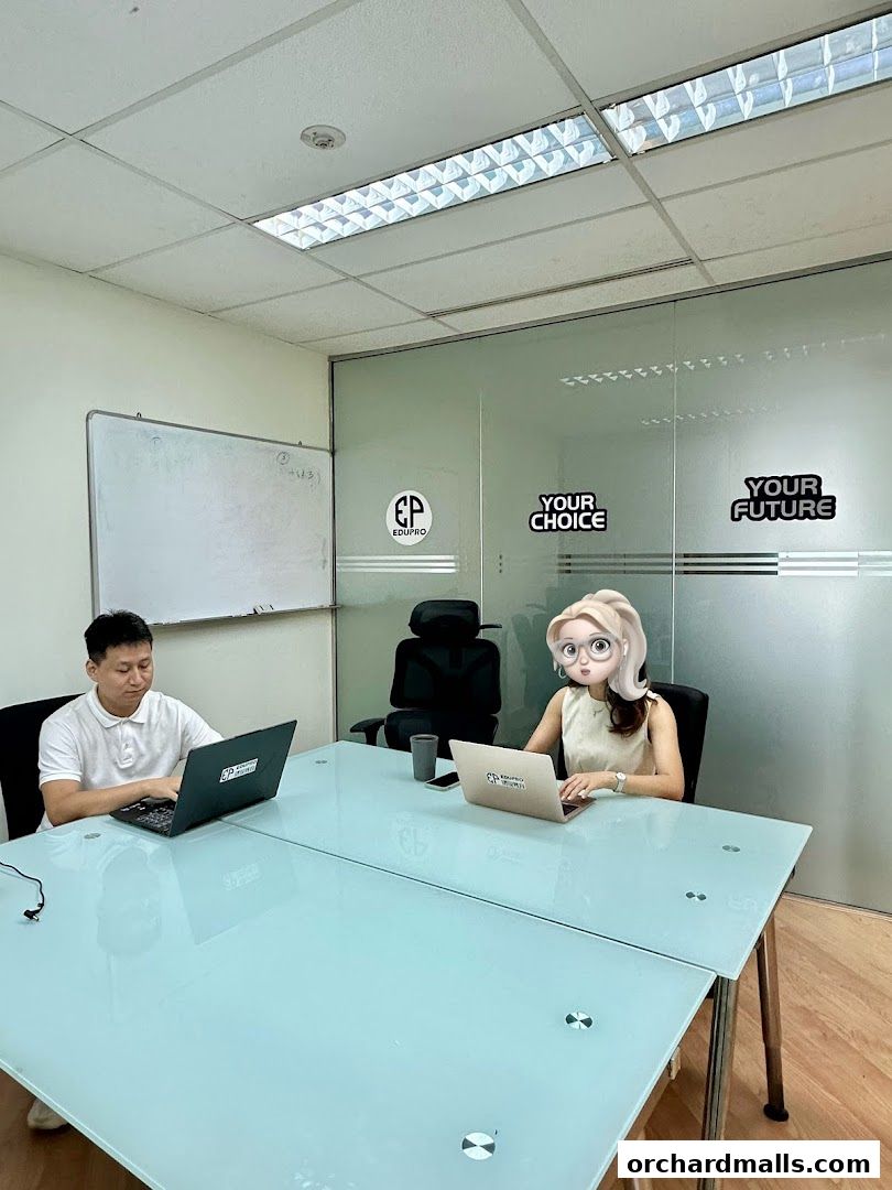 Two people working on laptops in a modern office with glass walls and motivational text.