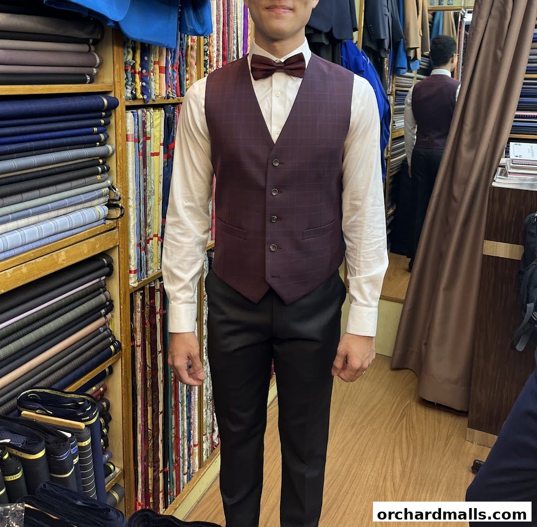 A man models a tailored vest and trousers in a fabric shop with rolls of cloth.