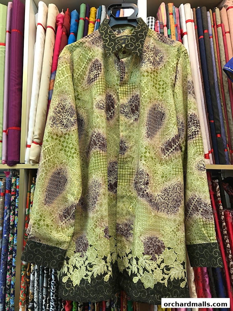 A batik-patterned shirt displayed in a tailor shop with fabric rolls in the background.