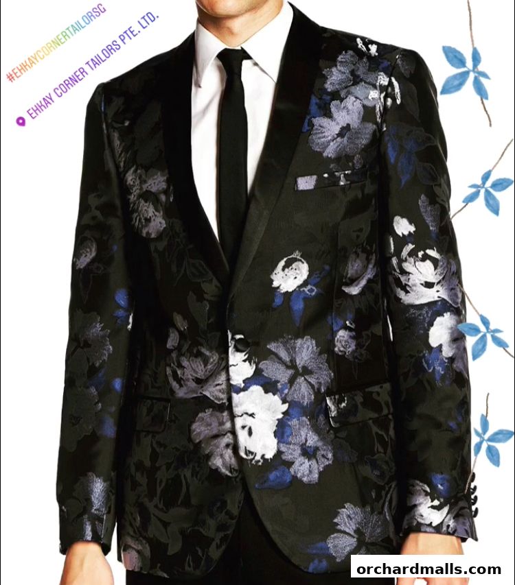 A man wearing a black floral patterned suit jacket with a white shirt and black tie.
