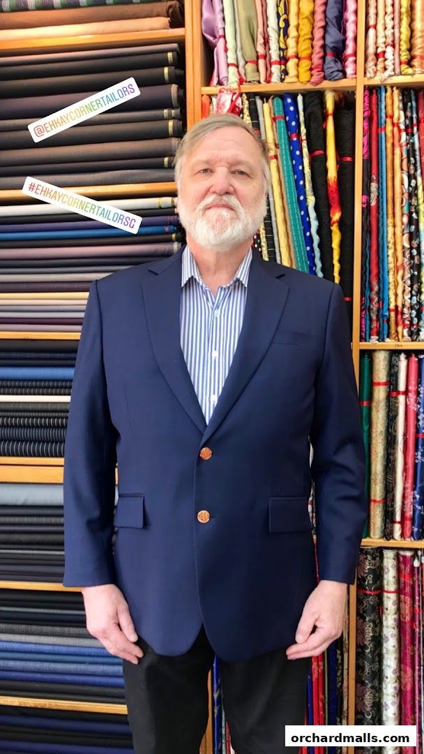 A man in a navy blue suit stands in front of shelves filled with fabric rolls.