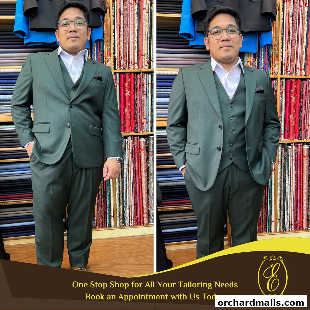 A man models a custom-tailored dark green suit in front of fabric rolls at Ehkay Corner Tailors.
