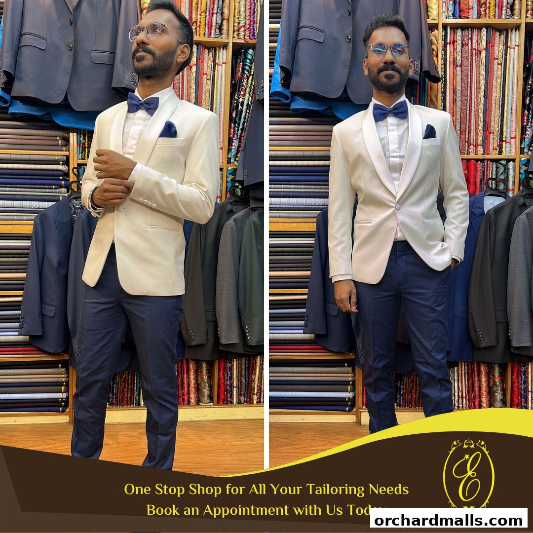 A man models a cream-colored tuxedo with navy blue pants and a blue bowtie in a tailor shop.