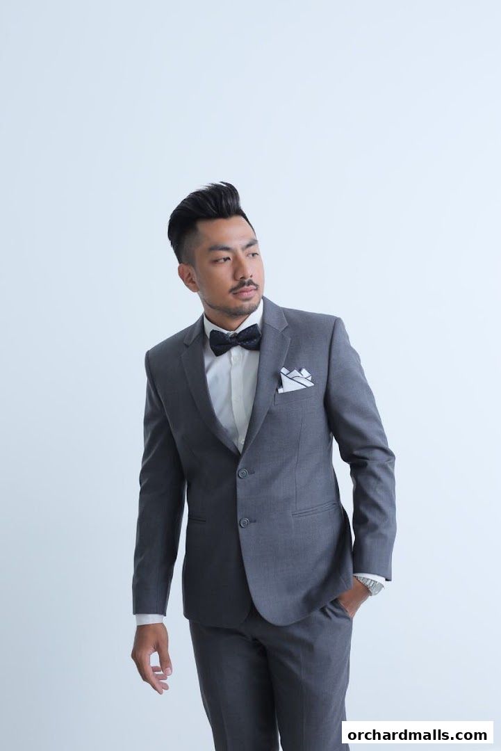 A man in a grey suit with a bow tie poses against a white background.