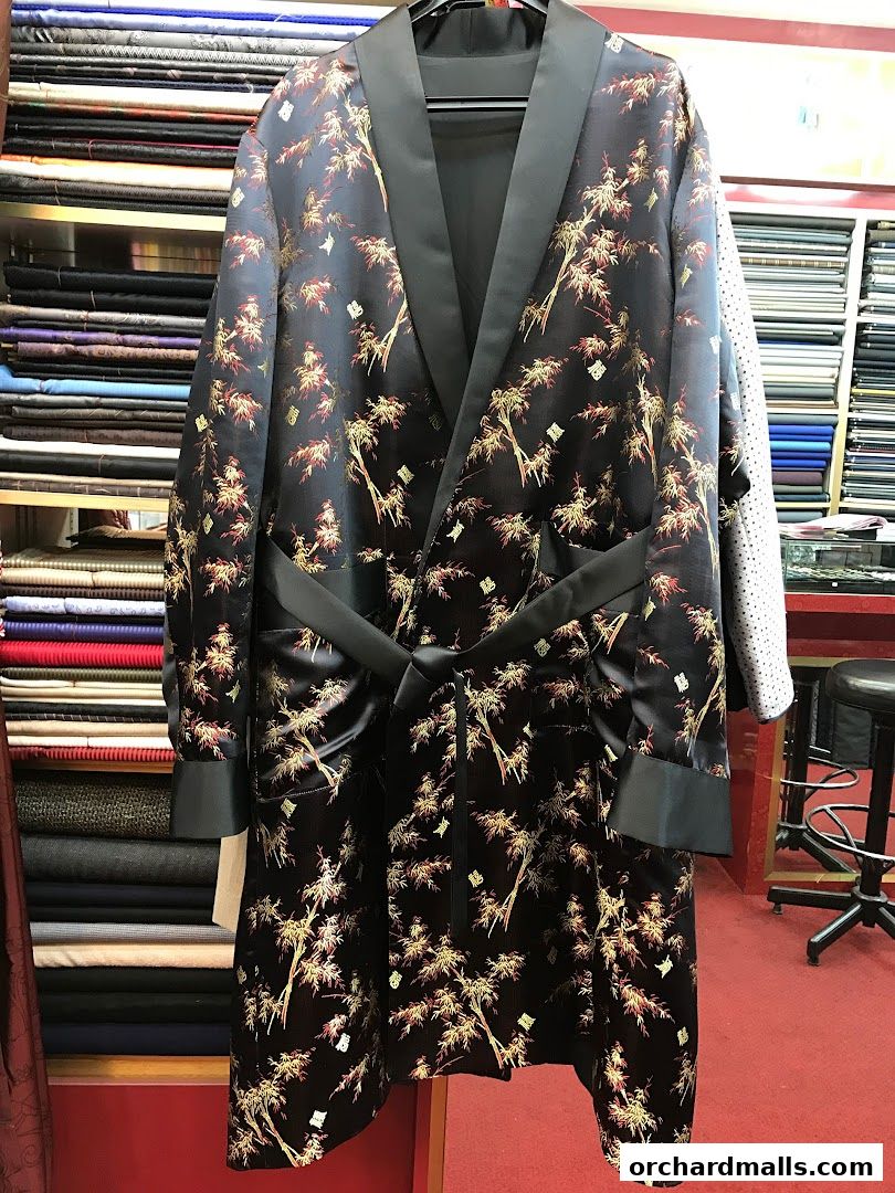 A stylish black robe with a bamboo pattern, displayed in a tailor shop with fabric rolls.