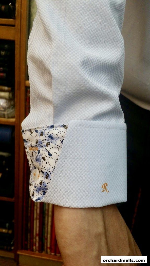 Close-up of a light blue dress shirt cuff with a patterned inner lining and an embroidered initial.