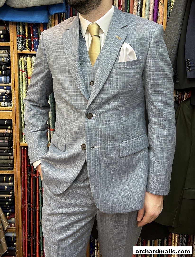 A man models a light blue plaid three-piece suit with a yellow tie and white pocket square.