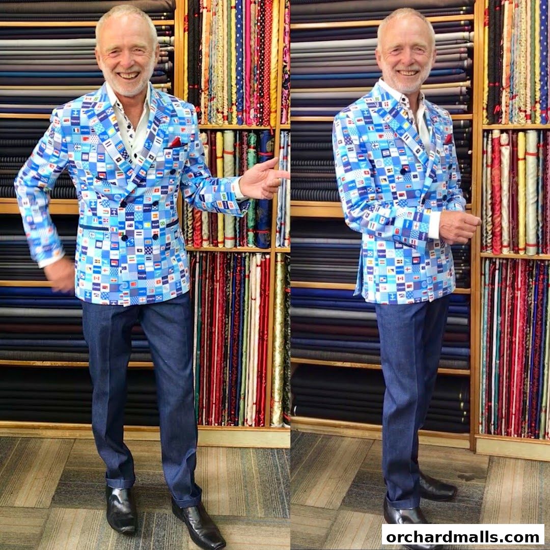 A tailor displays a unique double-breasted jacket with a flag pattern, surrounded by fabric rolls.