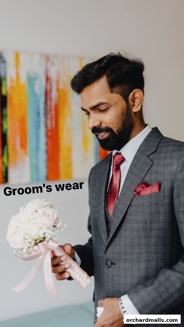 A man in a grey suit and red tie holds a bouquet of white and pink roses.